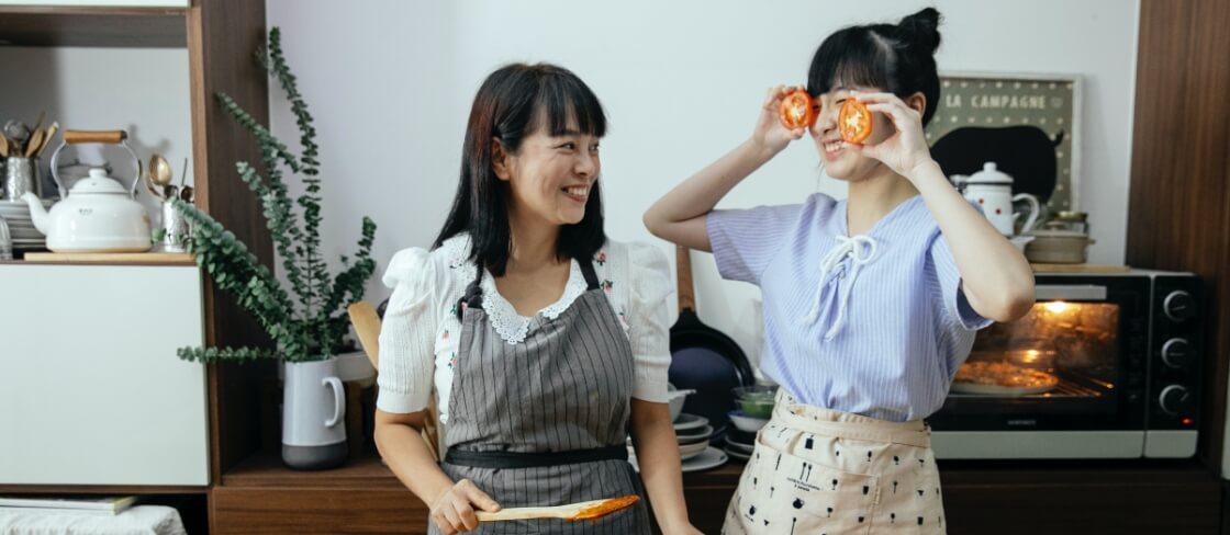 two women cooking with one holding slice tomatoes